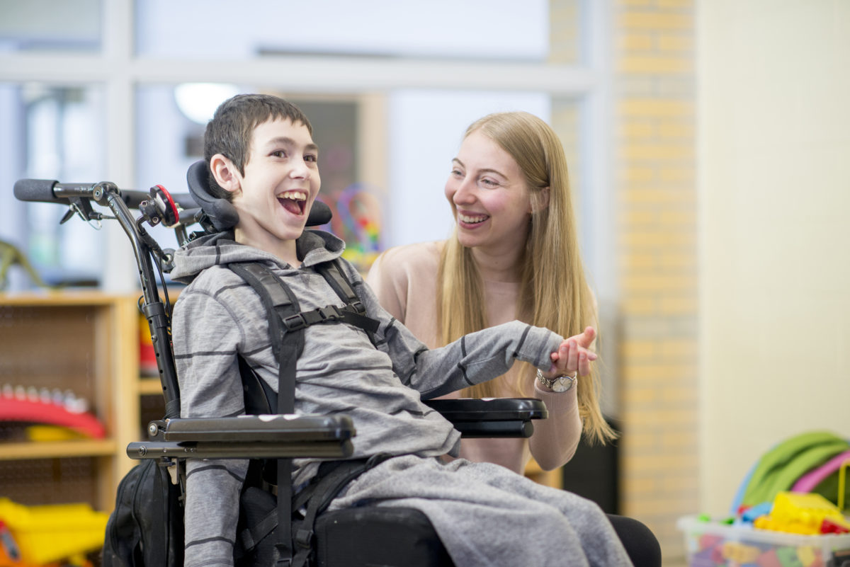 Bond Between Caregiver and Patient A caregiver is playing with a little boy that has a mental and physical disability. He is happily sitting in his wheelchair.